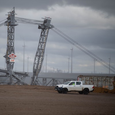 Das Bild zeigt einen Braunkohlebagger in der Nähe des ehemaligen Ortes Lützerath. Im Hintergrund sind Windräder zu erkennen.