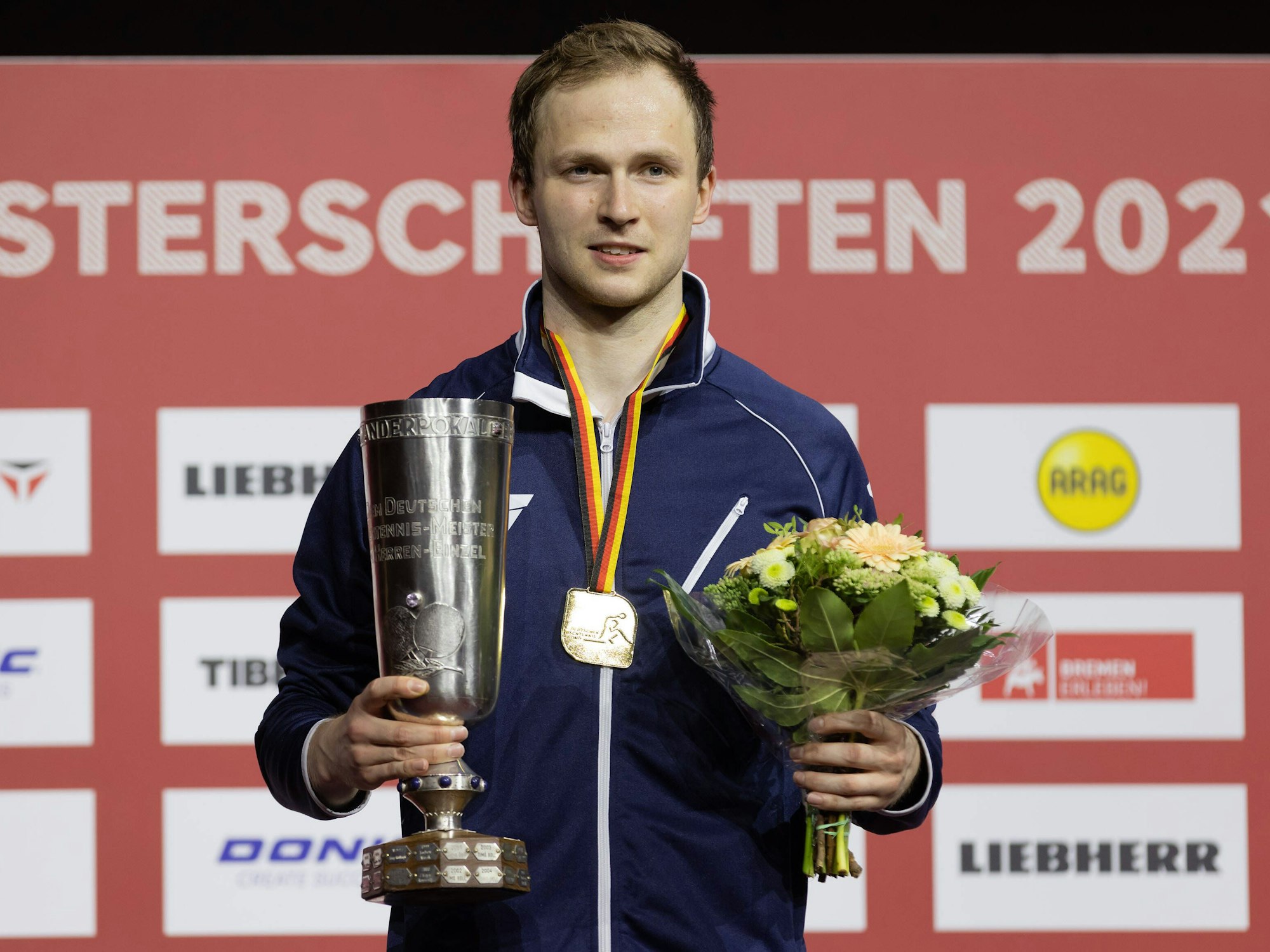 Benedikt Duda steht mit dem Meisterpokal und einem Blumenstrauß auf dem Siegerpodest.