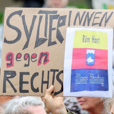 Teilnehmer halten bei einer Kundgebung Pappschilder hoch, darunter ein Schild mit dem Schriftzug „SylterInnen gegen Rechts“.