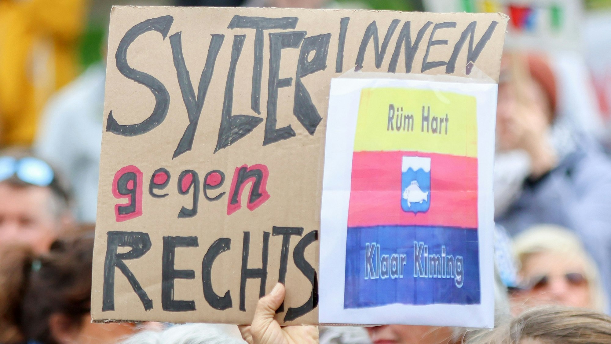Teilnehmer halten bei einer Kundgebung Pappschilder hoch, darunter ein Schild mit dem Schriftzug „SylterInnen gegen Rechts“.