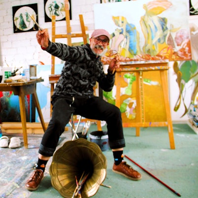 Ein Mann posiert mit einem Pinsel in der Hand in einem Maler-Atelier.