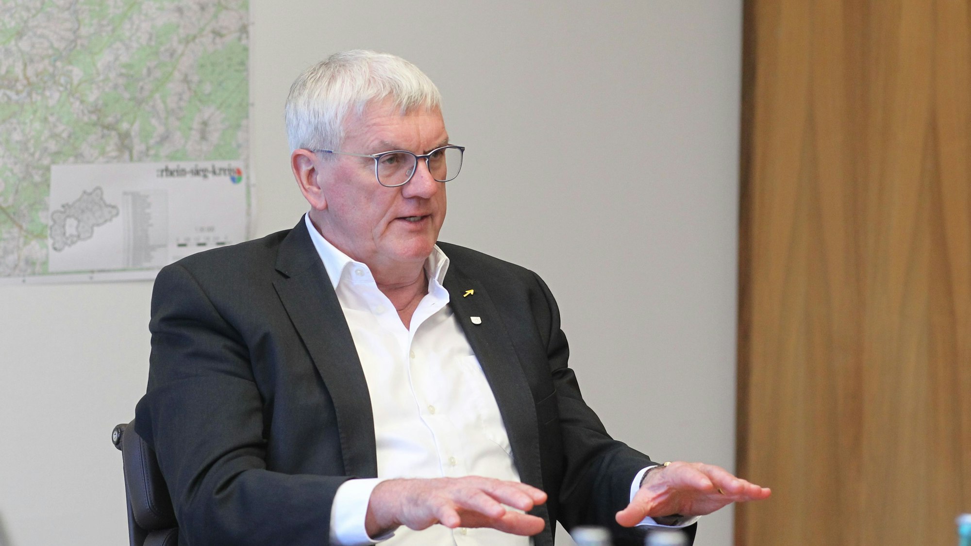 Landrat Sebastian Schusterin sitzt in seinem Büro im Siegburger Kreishaus vor einer großen Landkarte des Rhein-Sieg-Kreises.