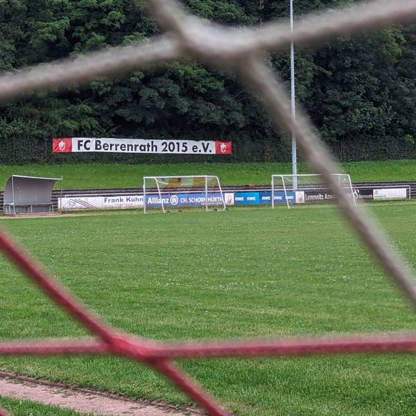 Das Foto zeigt den Naturrasenplatz in Berrenrath hinter den Maschen eines Tornetzes.