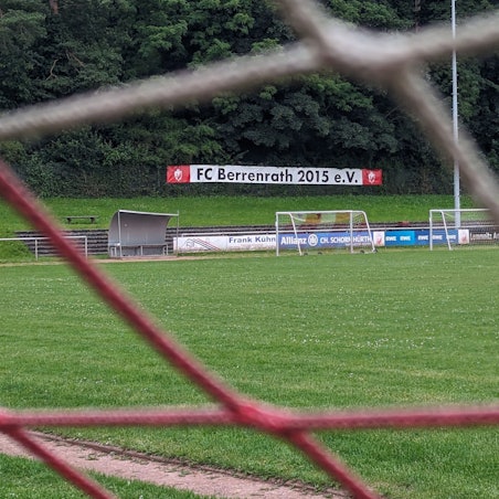 Das Foto zeigt den Naturrasenplatz in Berrenrath hinter den Maschen eines Tornetzes.