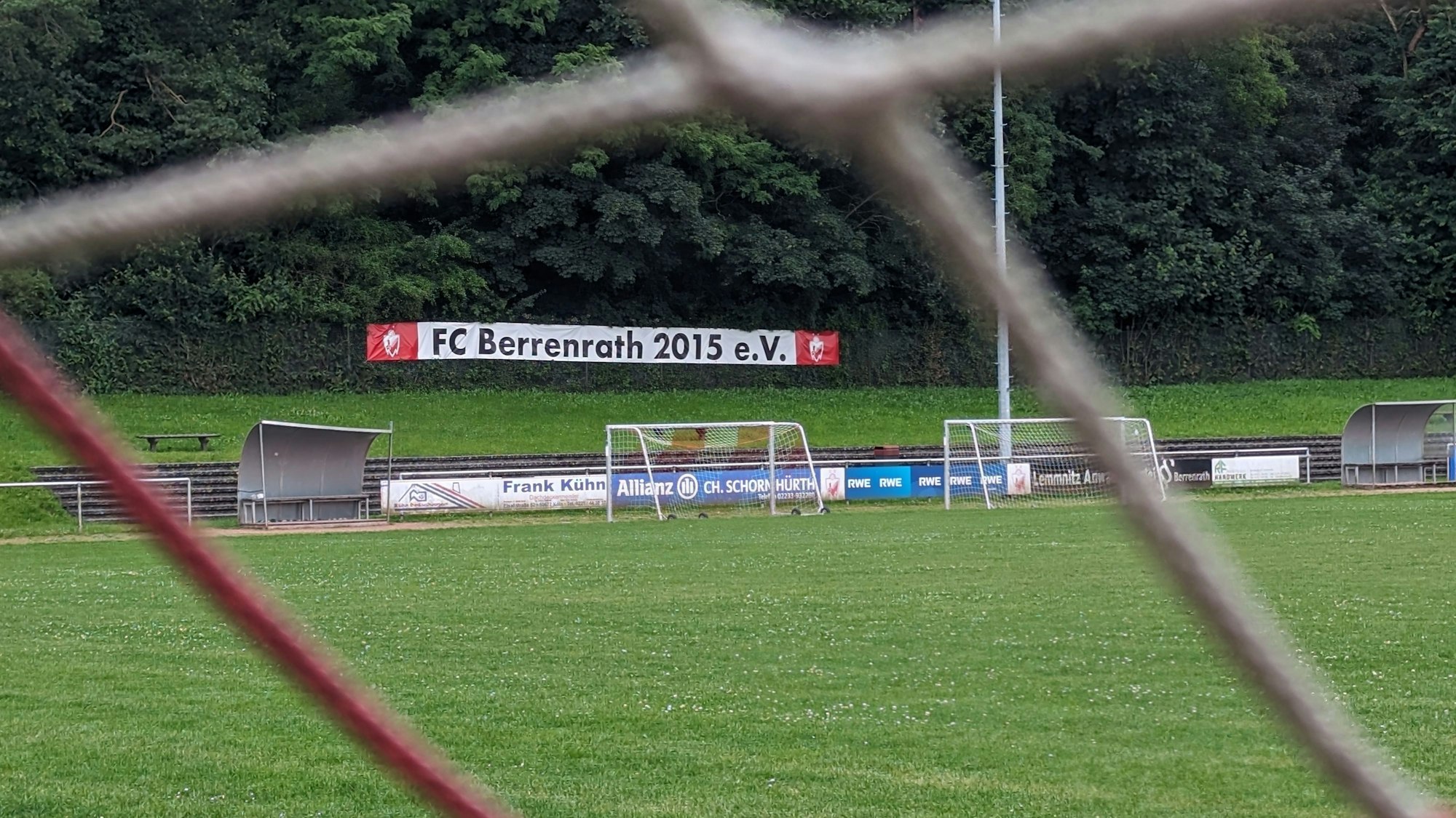 Das Foto zeigt den Naturrasenplatz in Berrenrath, fotografiert durch die Maschen eines Fußballtores.