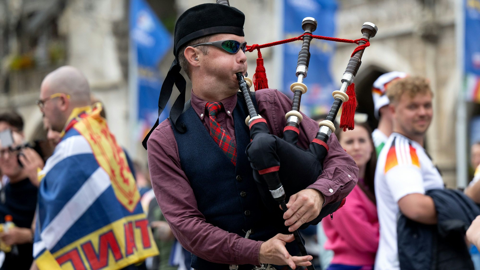 Ein schottischer Mann spielt Dudelsack, neben ihm andere Fußballfans mit Trikots und Flaggen.