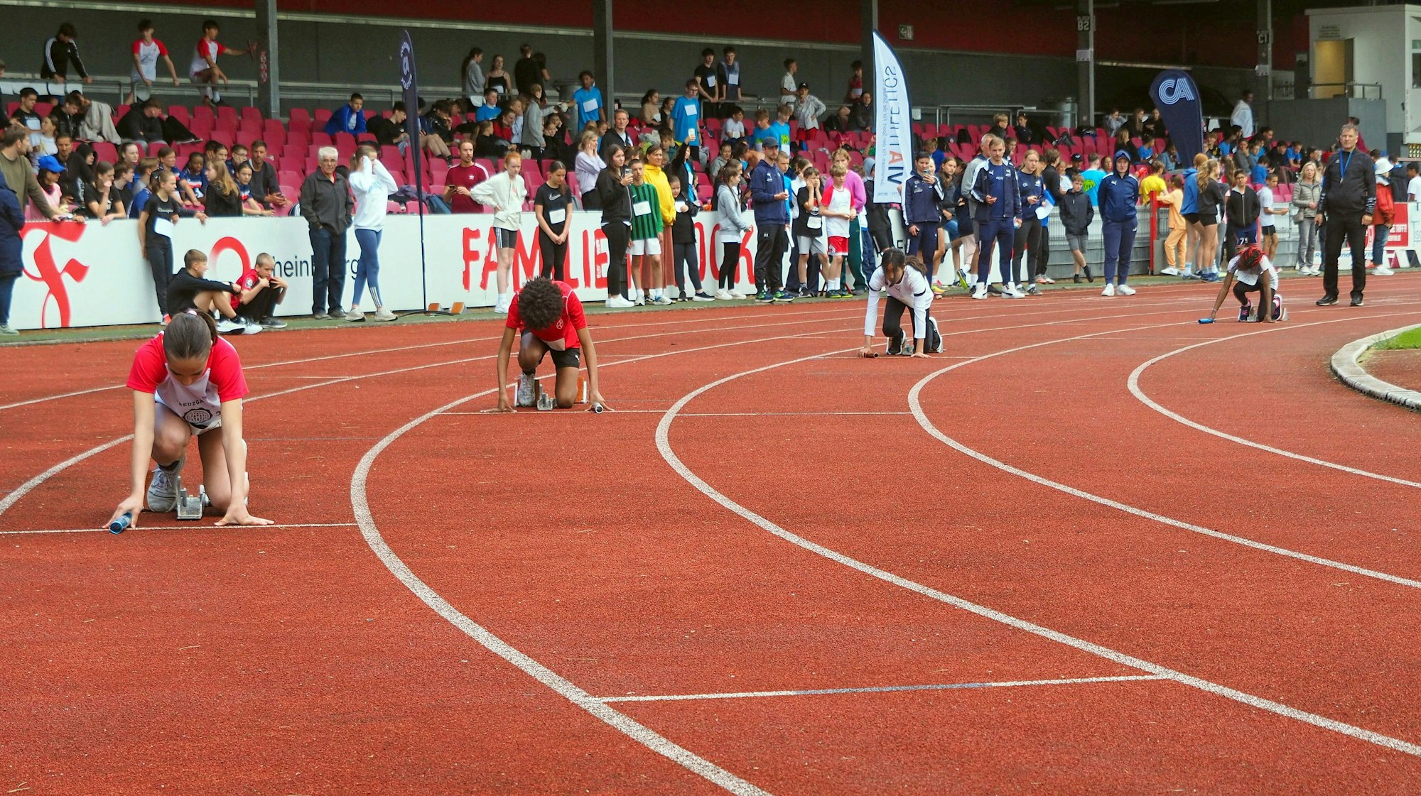 Blick auf die Laufbahn eines Stadions, vier Läufer kauern in den Startblöcken.