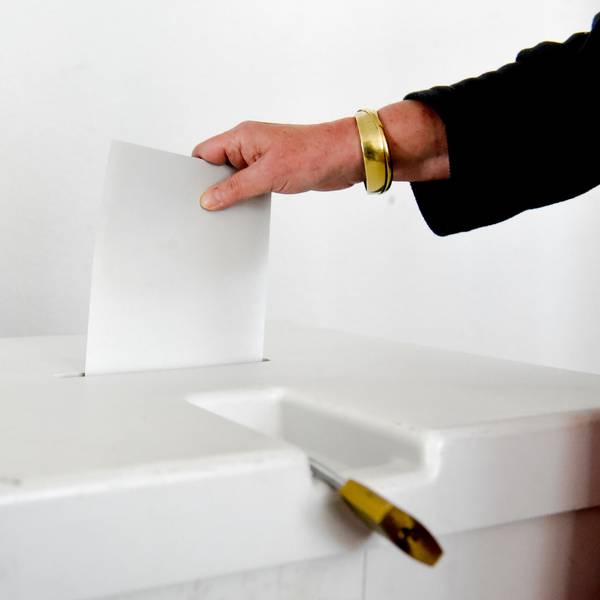 Eine Frauenhand wirft ein Blatt Papier in eine Wahlurne.