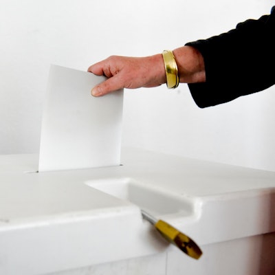 Eine Frauenhand wirft ein Blatt Papier in eine Wahlurne.