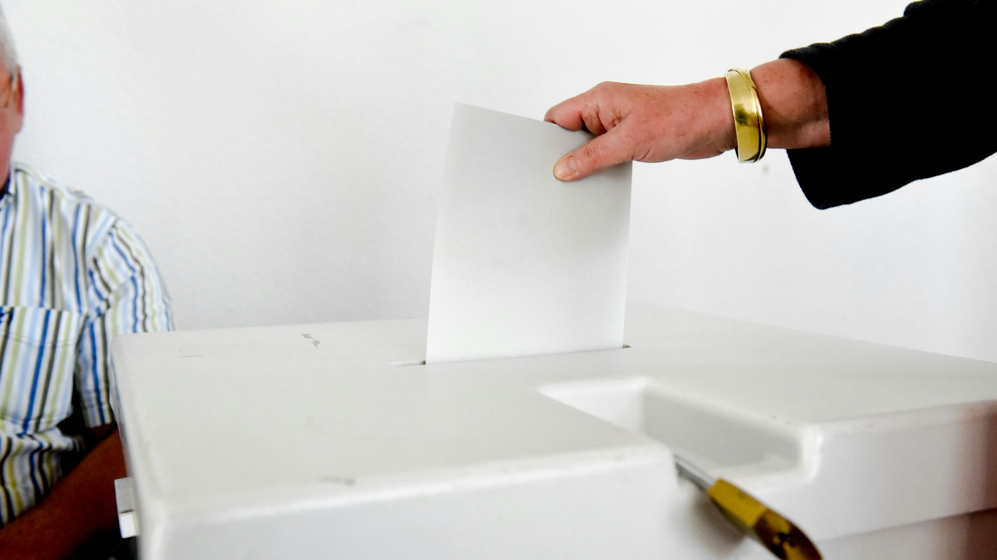Eine Frauenhand wirft ein Blatt Papier in eine Wahlurne.