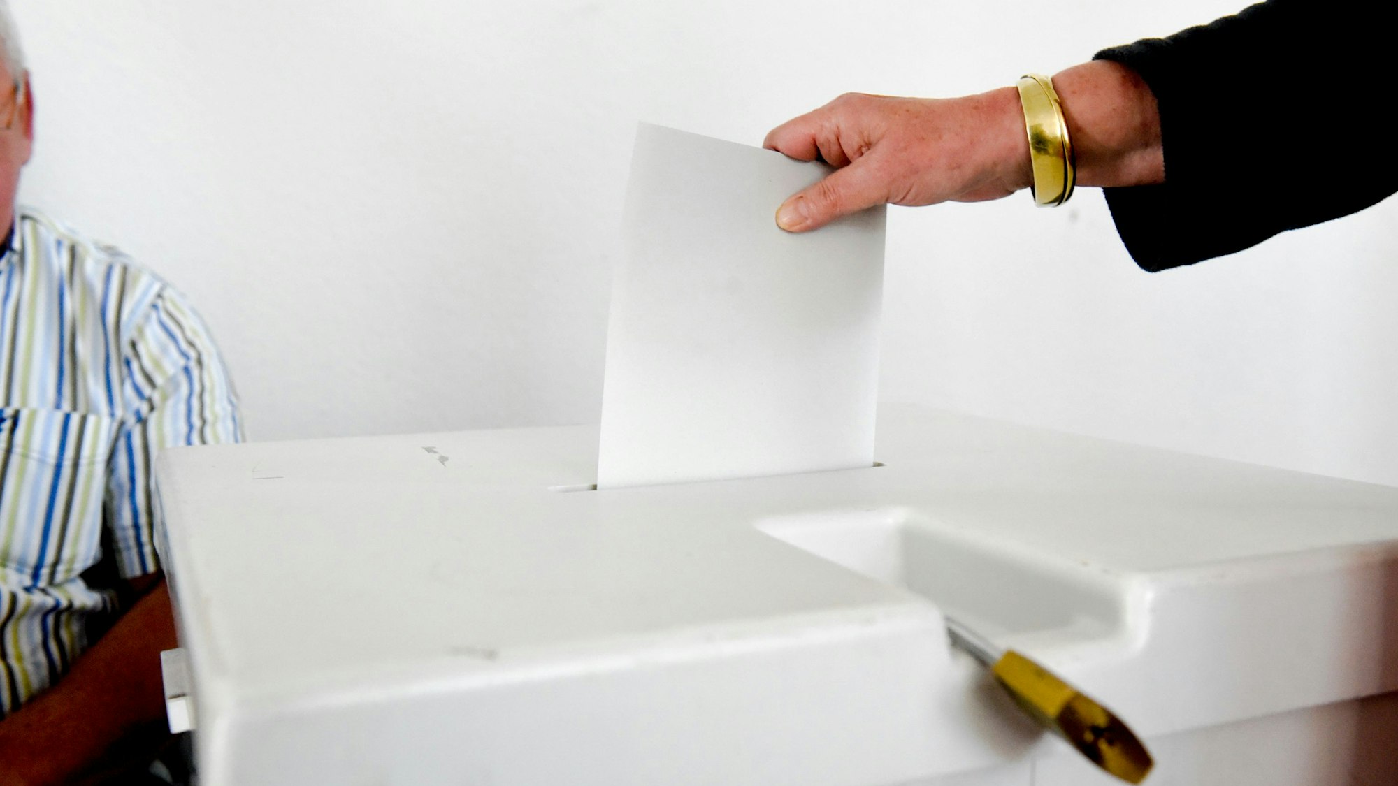 Zu sehen ist, wie eine Person einen Stimmzettel in einer Urne steckt.