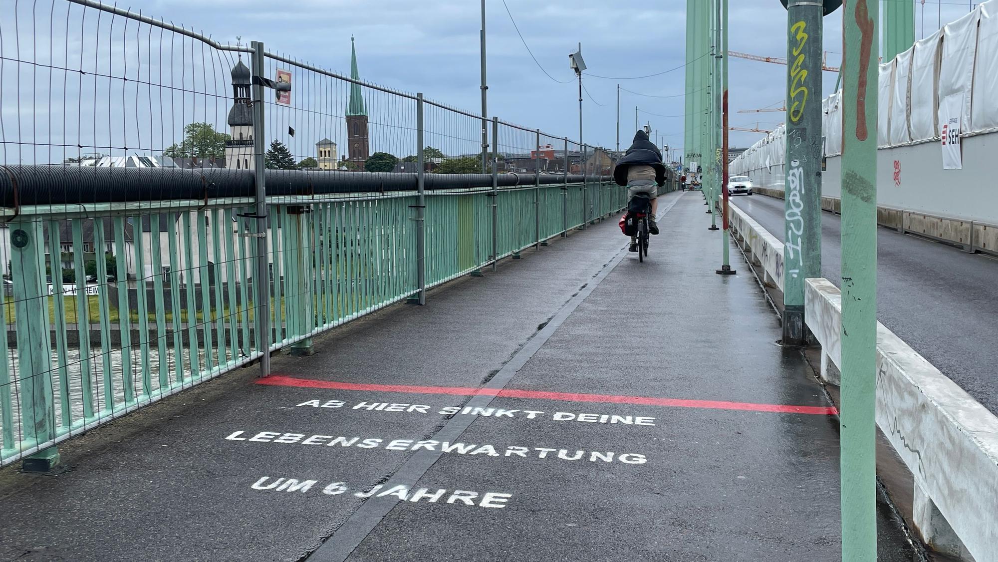 “Ab hier sinkt deine Lebenserwartung um 6 Jahre”: Dieser in Richtung der rechtsrheinischen Stadthälfte ausgerichtete Schriftzug ist seit Montag, dem 3. Juni auf Kölner Brücken zu sehen. Eine Analyse zeigt nun aber, dass die These nicht stimmt.