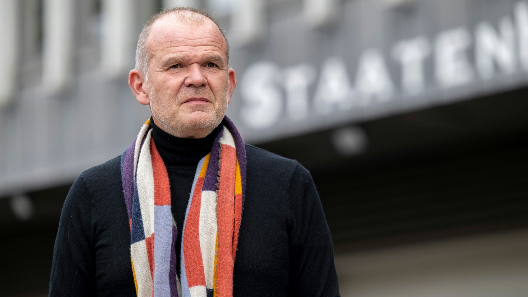 Francois-Xavier Roth steht vor dem Staatenhaus. Er trägt einen dunklen Pullover und darüber einen gemusterten Schal