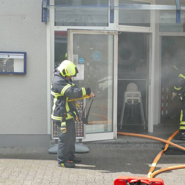 Rauch dringt aus dem Restauranteingang, in dem die Feuerwehrleute stehen.