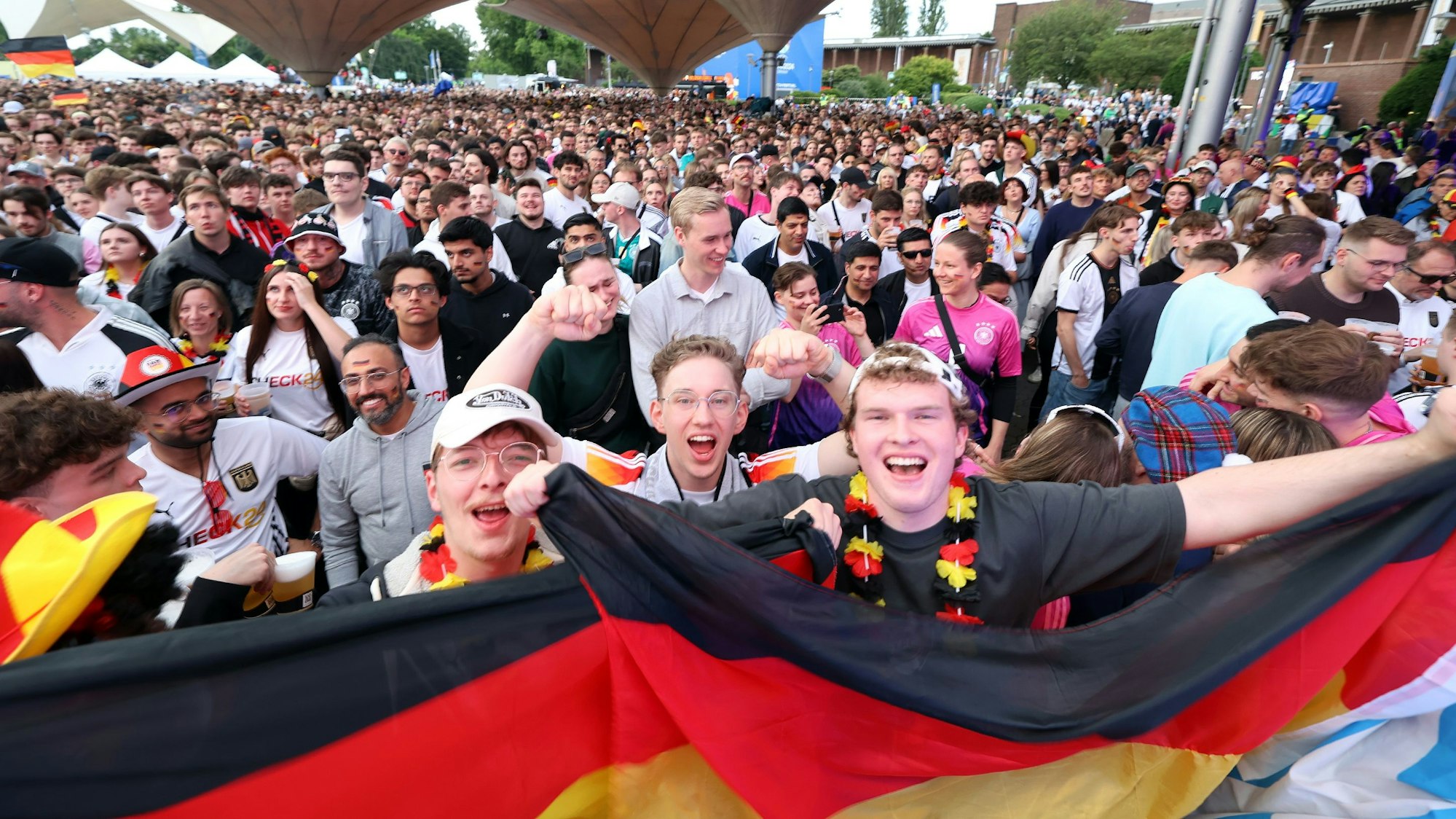 Fußballfans im Kölner Tanzbrunnen beim Public Viewing. Viele halten Deutschlandflaggen oder tragen die Trikots der Nationalmannschaft.