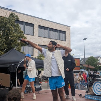 Die Bandmitglieder von Planschemalöör in weißen T-Shirts und blauen Hosen stehen auf der Bühne und singen mit den Demonstrierenden.