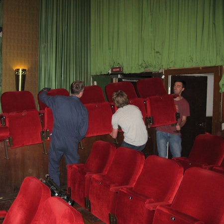 Vier Männer schleppen eine rote Kino-Klappsesselreihe aus dem Kinosaal.