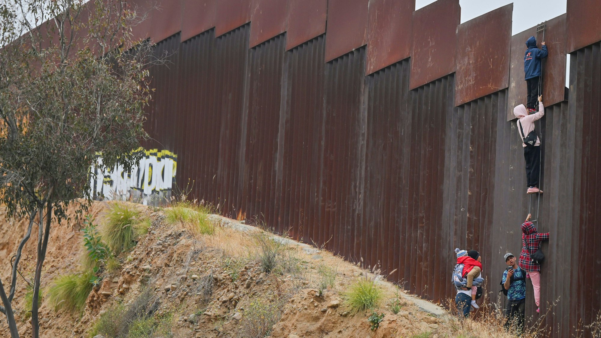 Migranten versuchen, von Mexiko aus mit einem Leiter über die Grenzmauer in die USA zu gelangen.