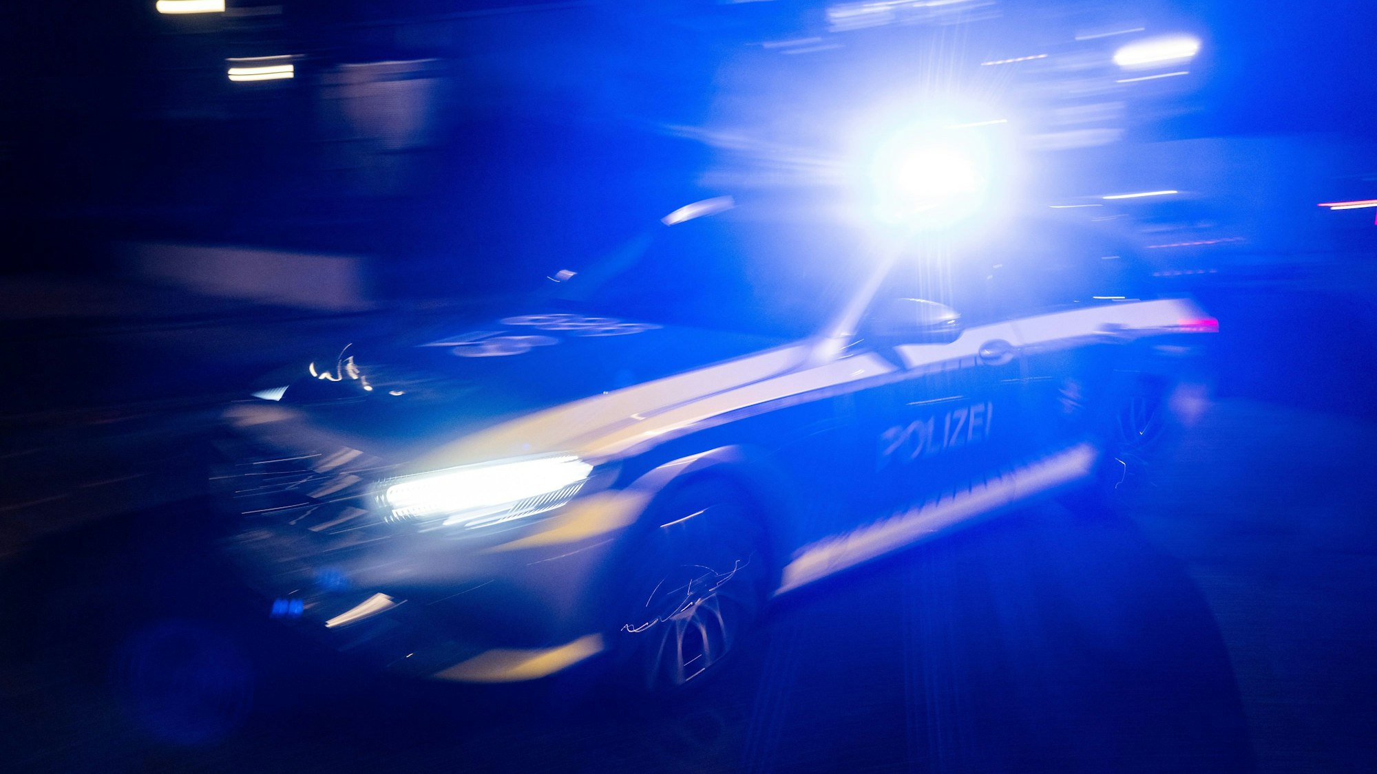 Ein Polizeifahrzeug fährt mit Blaulicht an einem Gebäude vorbei