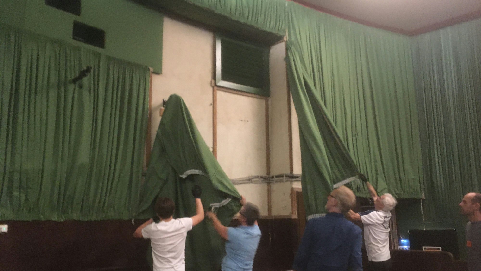 Mehrere Personen reißen den alten, grünen Wandbehang von den Kinowänden.