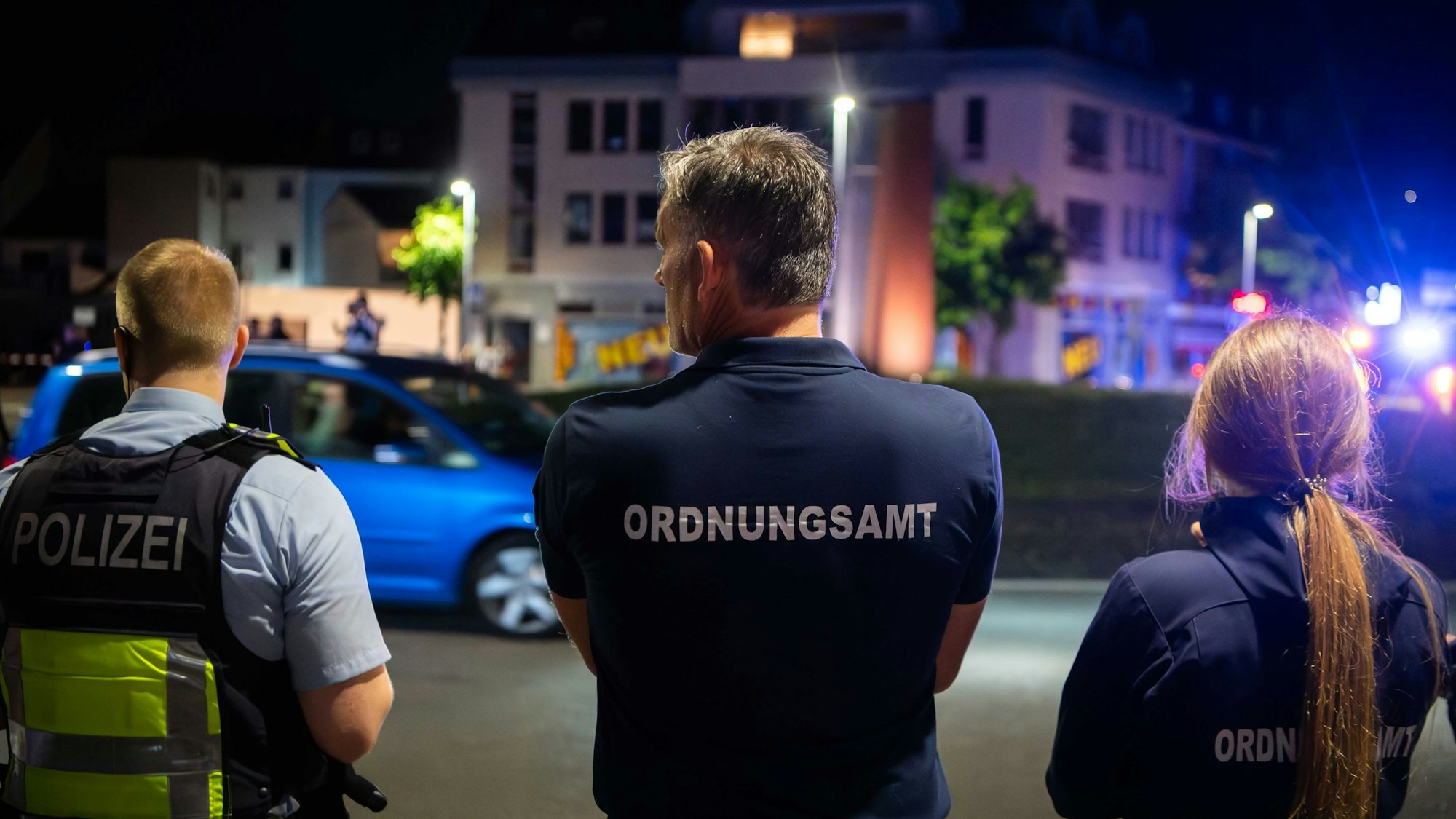 Zwei Männer und eine Frau sind von hinten zu sehen, wie sie das Geschehen auf dem Europakreisel beobachten. Einer trägt eine Polizeiweste, die beiden anderen haben die Aufschrift „Ordnungsamt“ auf dem Rücken stehen.