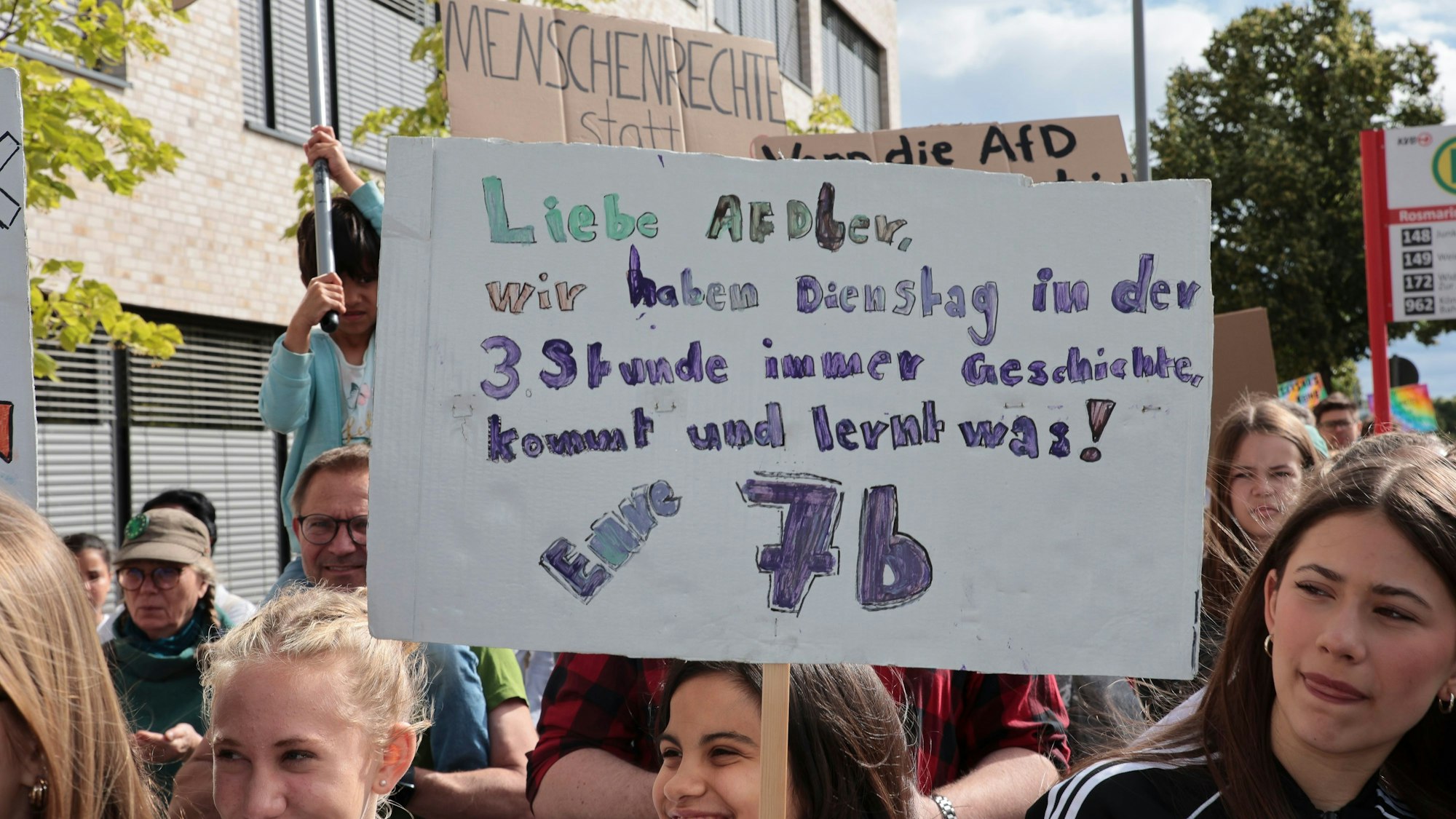 Schülerinnen halten ein Schild hoch mit einem Schriftzug, der die AfD auffordert, in ihren Geschichtsunterricht zu kommen und etwas zu lernen.
