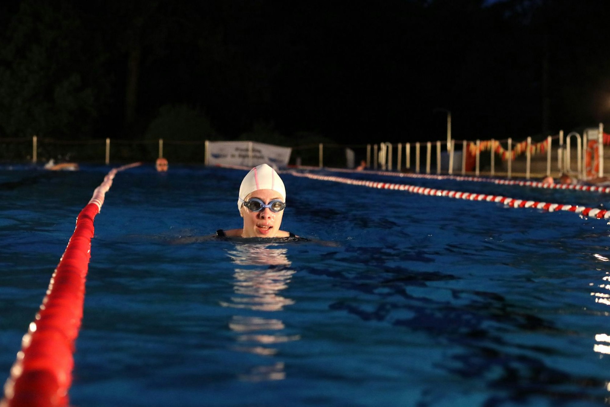 Eine Frau schwimmt bei Nacht, sie trägt eine Badekappe und eine Chlorbrille.