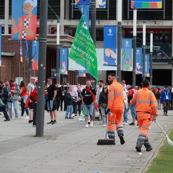 Zwei Mitarbeiter der AWB laufen zwischen Fußballfans umher und kehren Müll auf dem Weg vor dem Stadion zusammen.