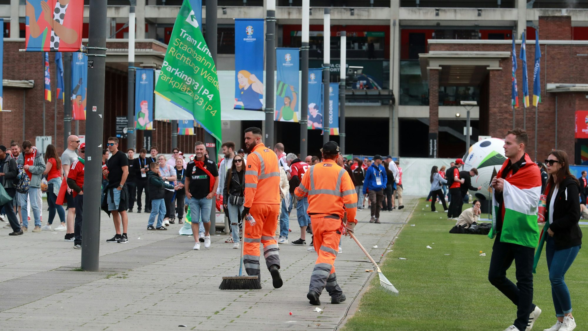 Zwei Mitarbeiter der AWB laufen zwischen Fußballfans umher und kehren Müll auf dem Weg vor dem Stadion zusammen.