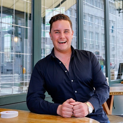 Ein junger Mann steht lachend an einem Stehtisch.