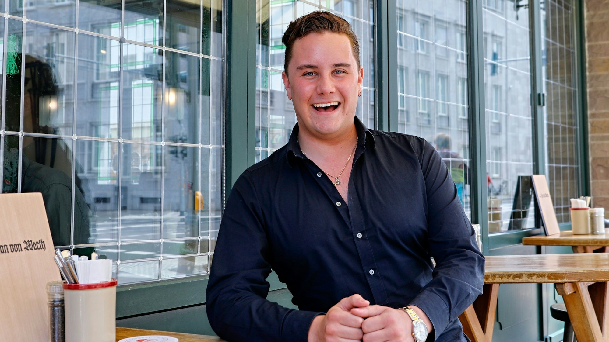 Ein junger Mann steht lachend an einem Stehtisch.