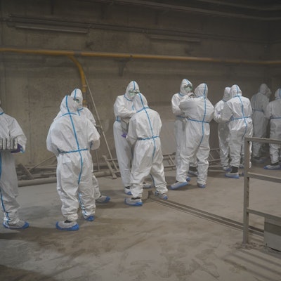 Menschen in weißen Schutzanzügen haben eine Kette gebildet vor dem Verbrennungsofen und reichen Drogenpakete durch.