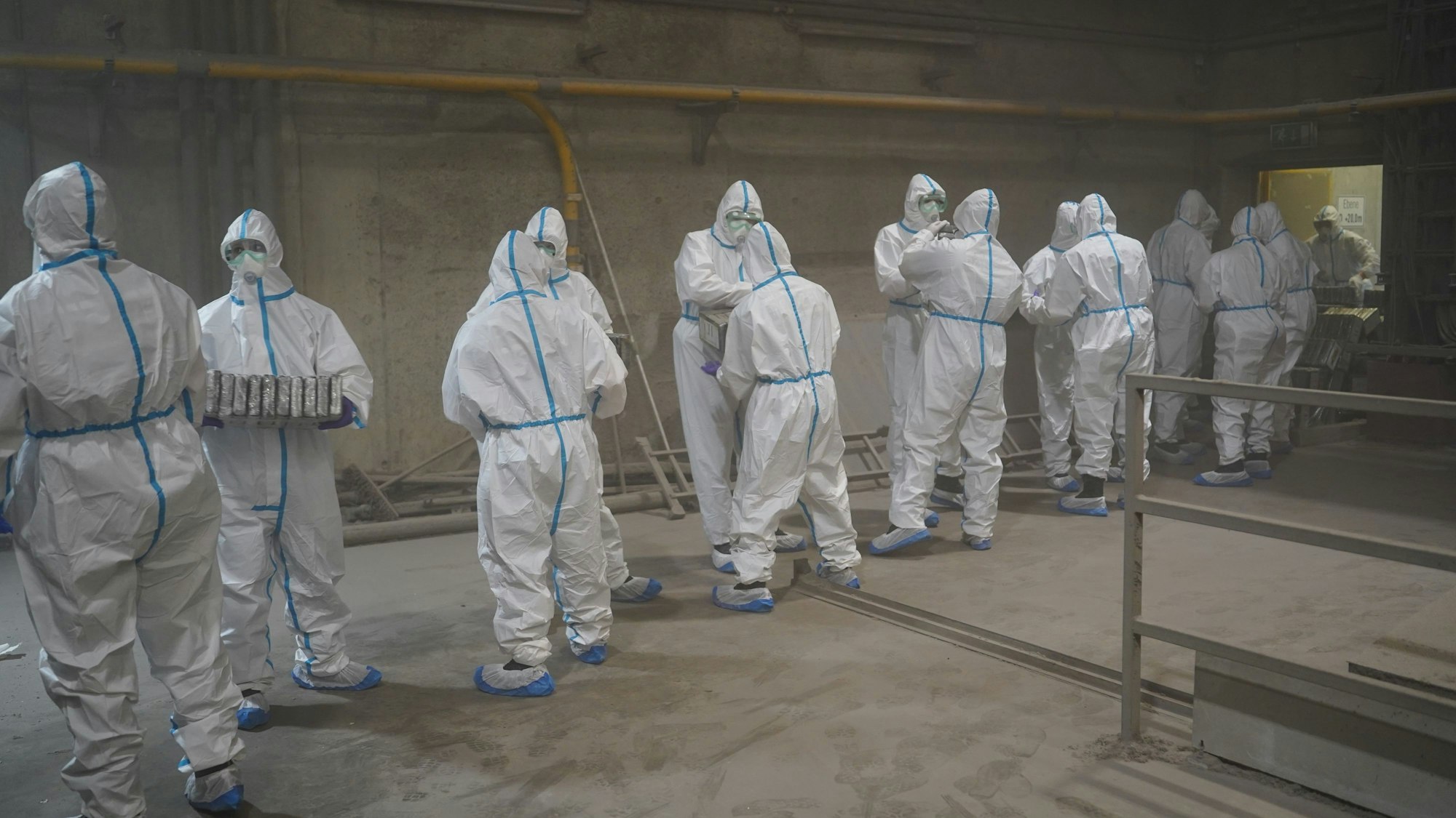 Menschen in weißen Schutzanzügen haben eine Kette gebildet vor dem Verbrennungsofen und reichen Drogenpakete durch.