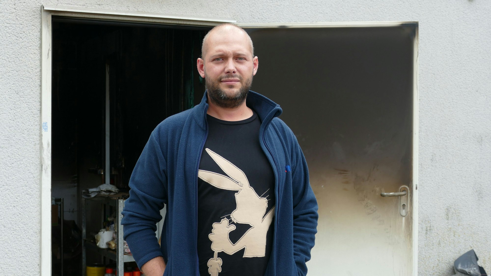 Ein Mann steht vor der schwarz verkohlten Eingangstür.