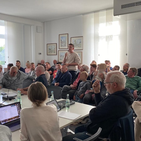 Im Publikum steht ein Anwohner mit Mikrofon. Die Ratsmitglieder hören zu.