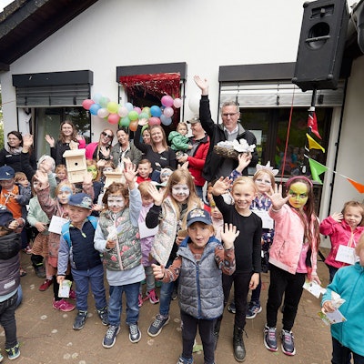 Kinder und Erwachsene stehen vor dem Kita-Gebäude, das mit Ballons und Wimpeln geschmückt ist.