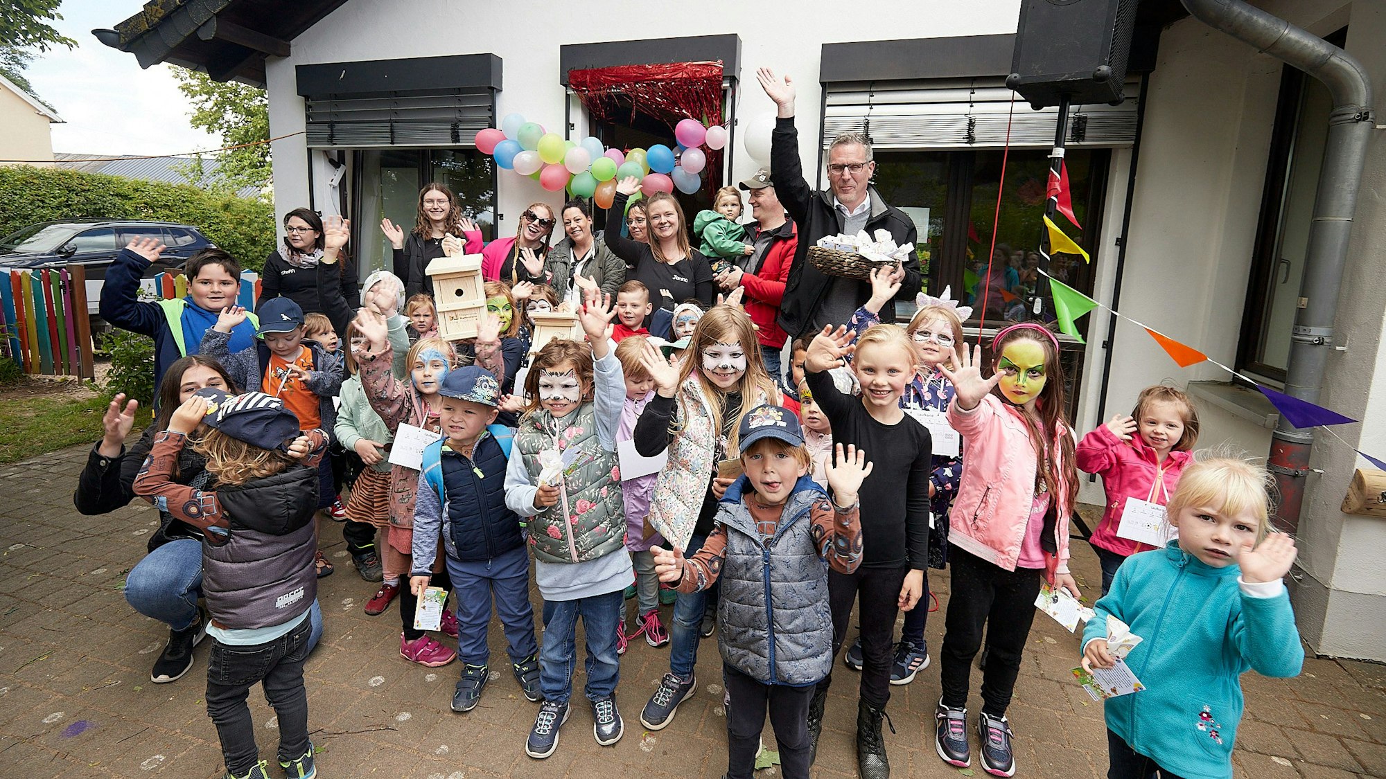 Kinder und Erwachsene stehen vor dem Kita-Gebäude, das mit Ballons und Wimpeln geschmückt ist.