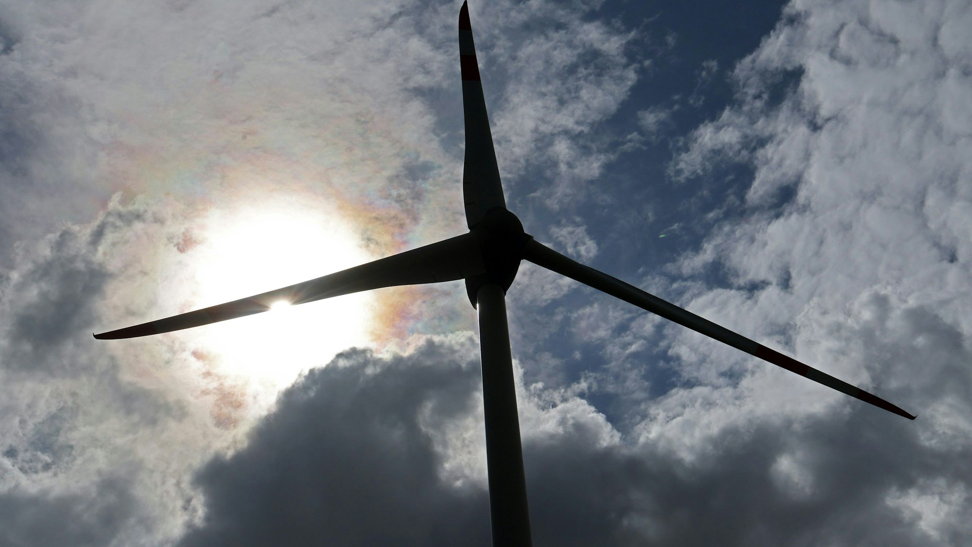 Eine Windkraftanlage ist vor einem leicht bewölktem Himmel im Gegenlicht zu sehen.