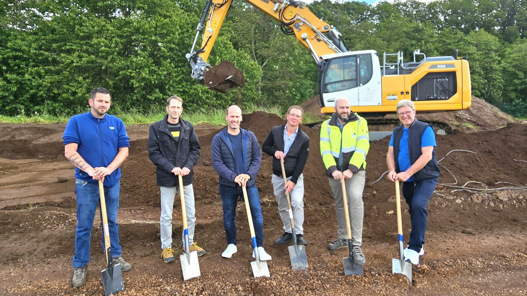 Marc Hees (v.l.), Stefan Jovy, Markus Auel, Mike Breitegger, Christoph Graf und Manfred Poth stehen mit Spaten vor einem Bagger.