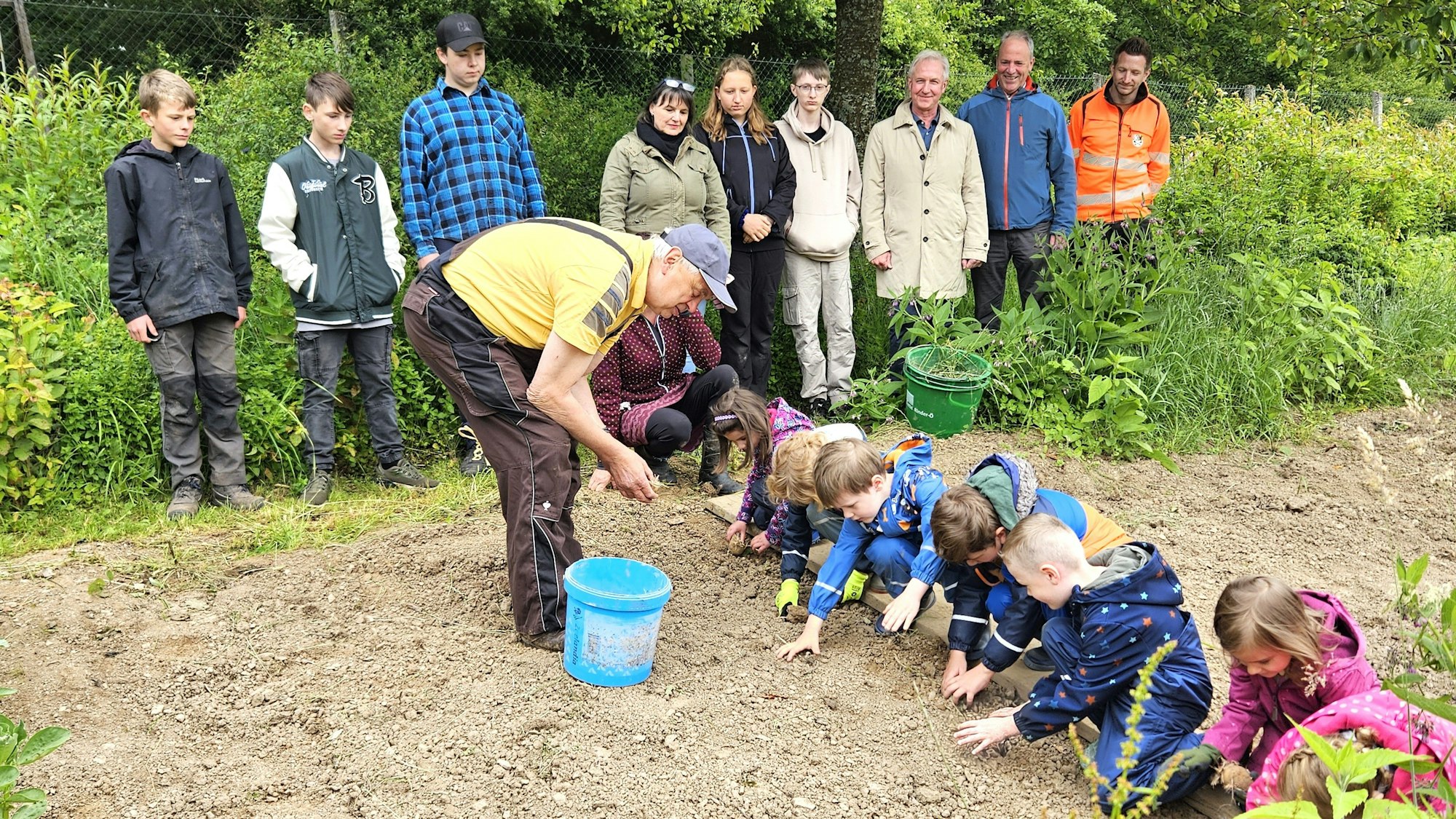 Rudi Diefenbach steht in einem Beet, die Kinder hocken vor ihm und setzen Kartoffeln.
