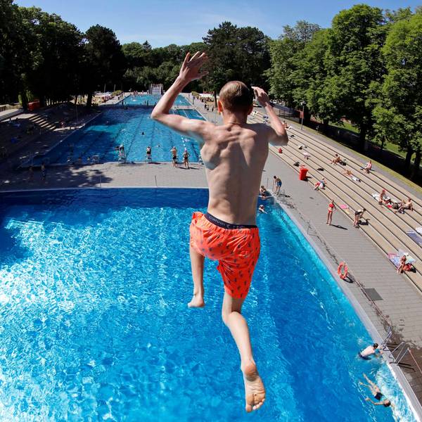 Zu sehen ist ein Badegast in der Rückansicht, der in einem Freibad aus 7,5 Metern Höhe ins Wasser springt.