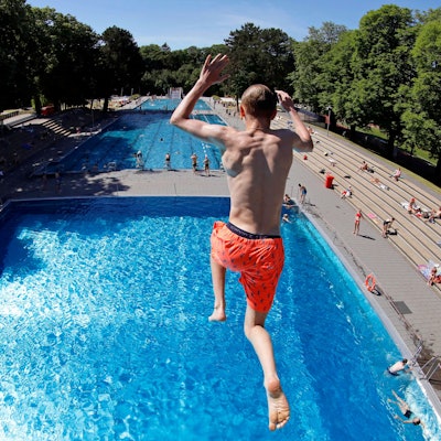 Zu sehen ist ein Badegast in der Rückansicht, der in einem Freibad aus 7,5 Metern Höhe ins Wasser springt.