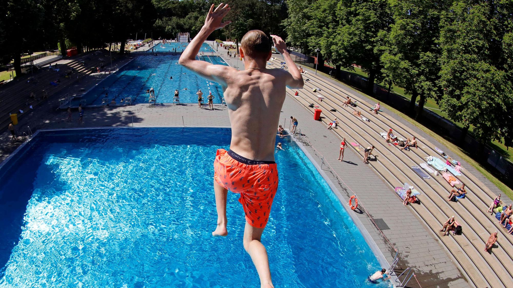 Zu sehen ist ein Badegast in der Rückansicht, der in einem Freibad aus 7,5 Metern Höhe ins Wasser springt.