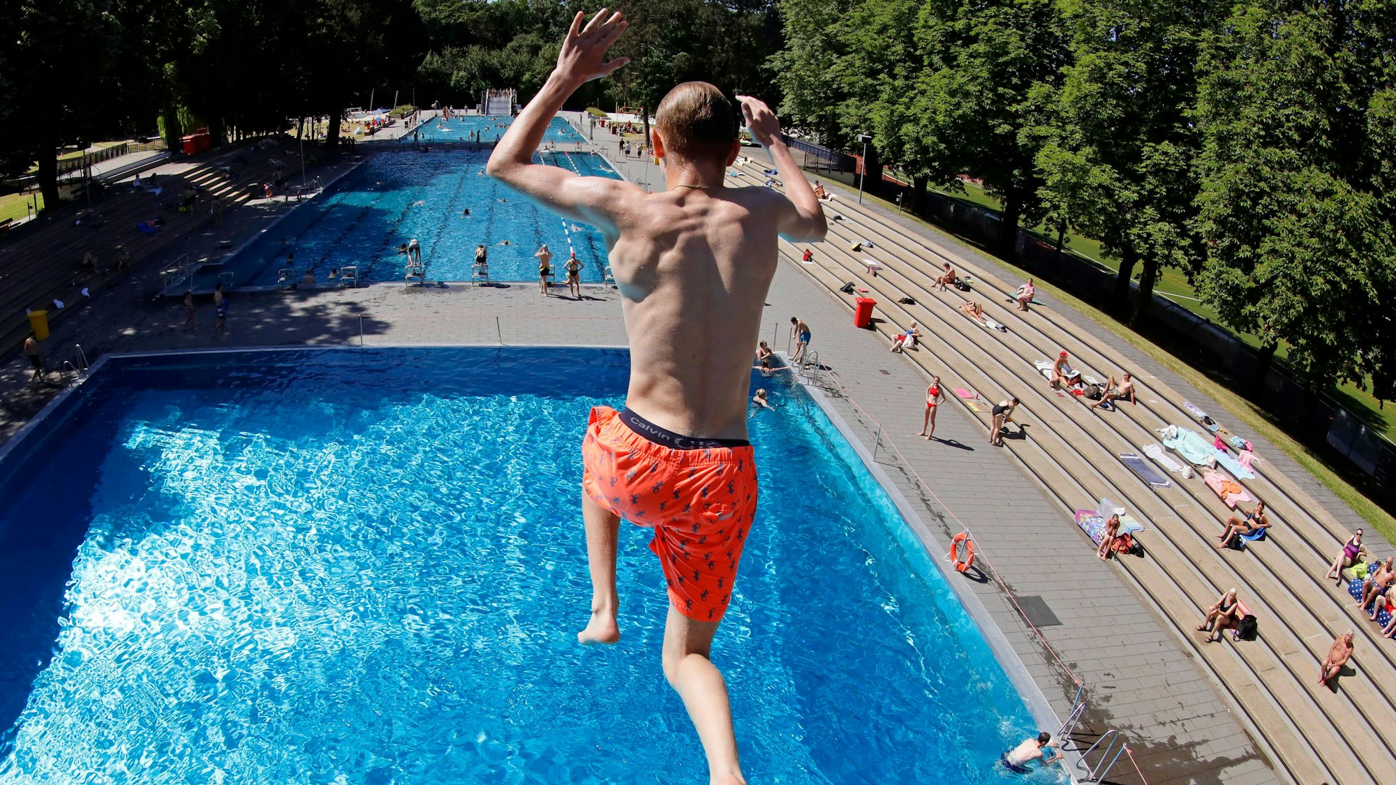Zu sehen ist ein Badegast in der Rückansicht, der in einem Freibad aus 7,5 Metern Höhe ins Wasser springt.