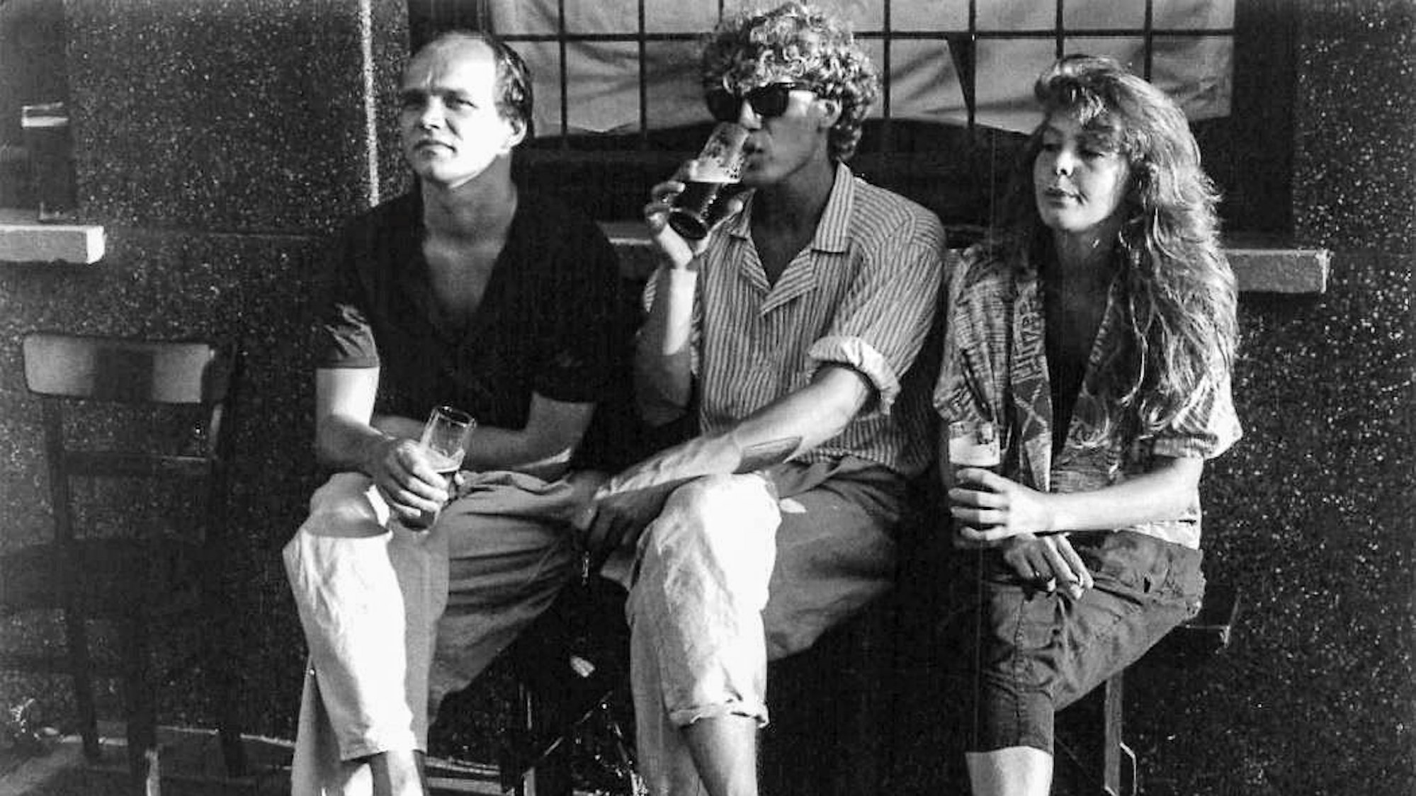 Zwei Männer und eine Frau auf einer Bank vor einer Kneipe