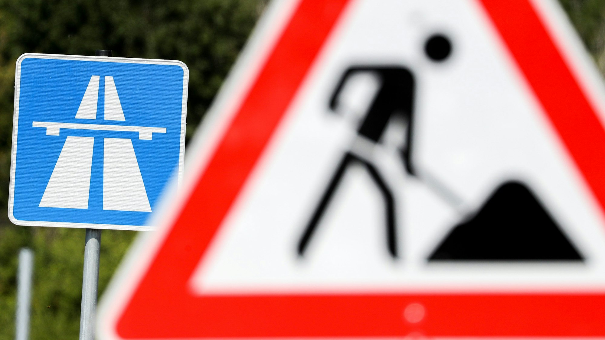 Auf dem Foto sind ein Baustellenschild zu sehen, dahinter weist ein anderes Schild auf die Autobahn.
