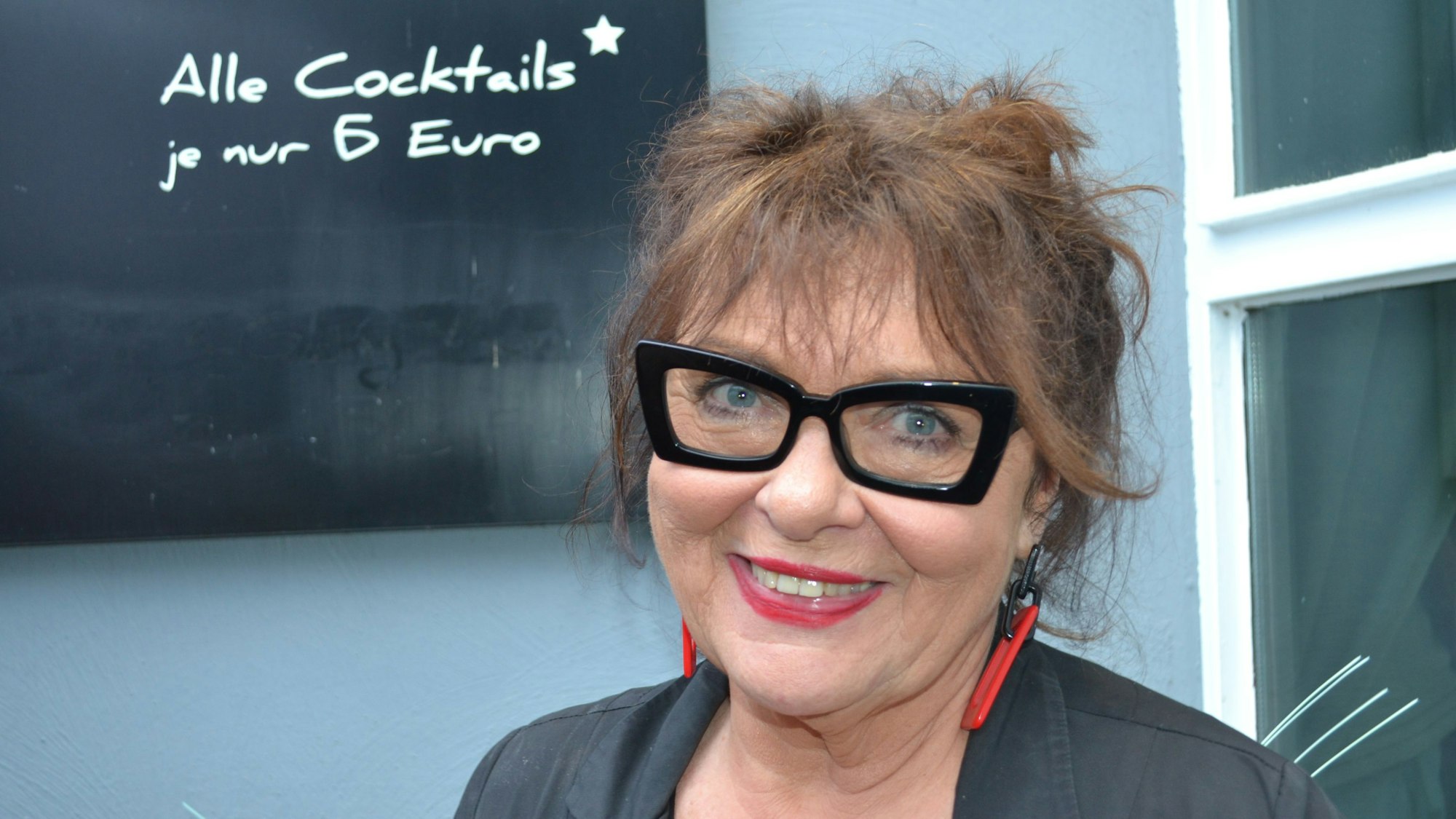 Eine Frau vor einer Schiefertafel mit Aufschrift alle Cocktails je nur 6 Euro