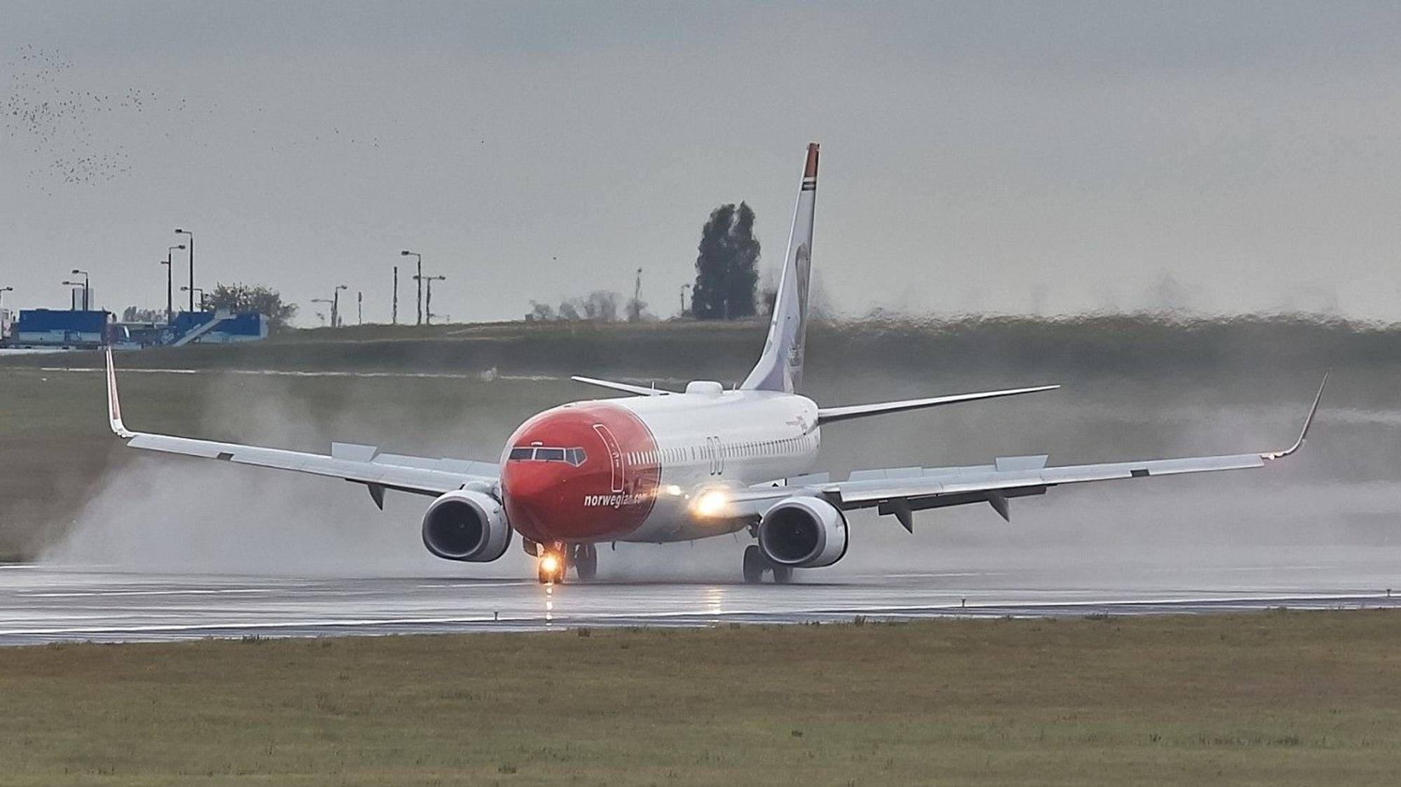 Eine Boeing 737 der norwegischen Fluggesellschaft Norwegian landet während eines Gewitters auf einer Landebahn. Regen spritzt von der Landebahn nach oben. (Archivbild)
