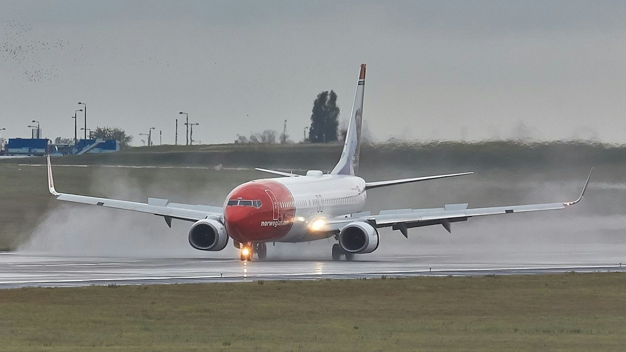 Eine Boeing 737 der norwegischen Fluggesellschaft Norwegian landet während eines Gewitters auf einer Landebahn. Regen spritzt von der Landebahn nach oben. (Archivbild)