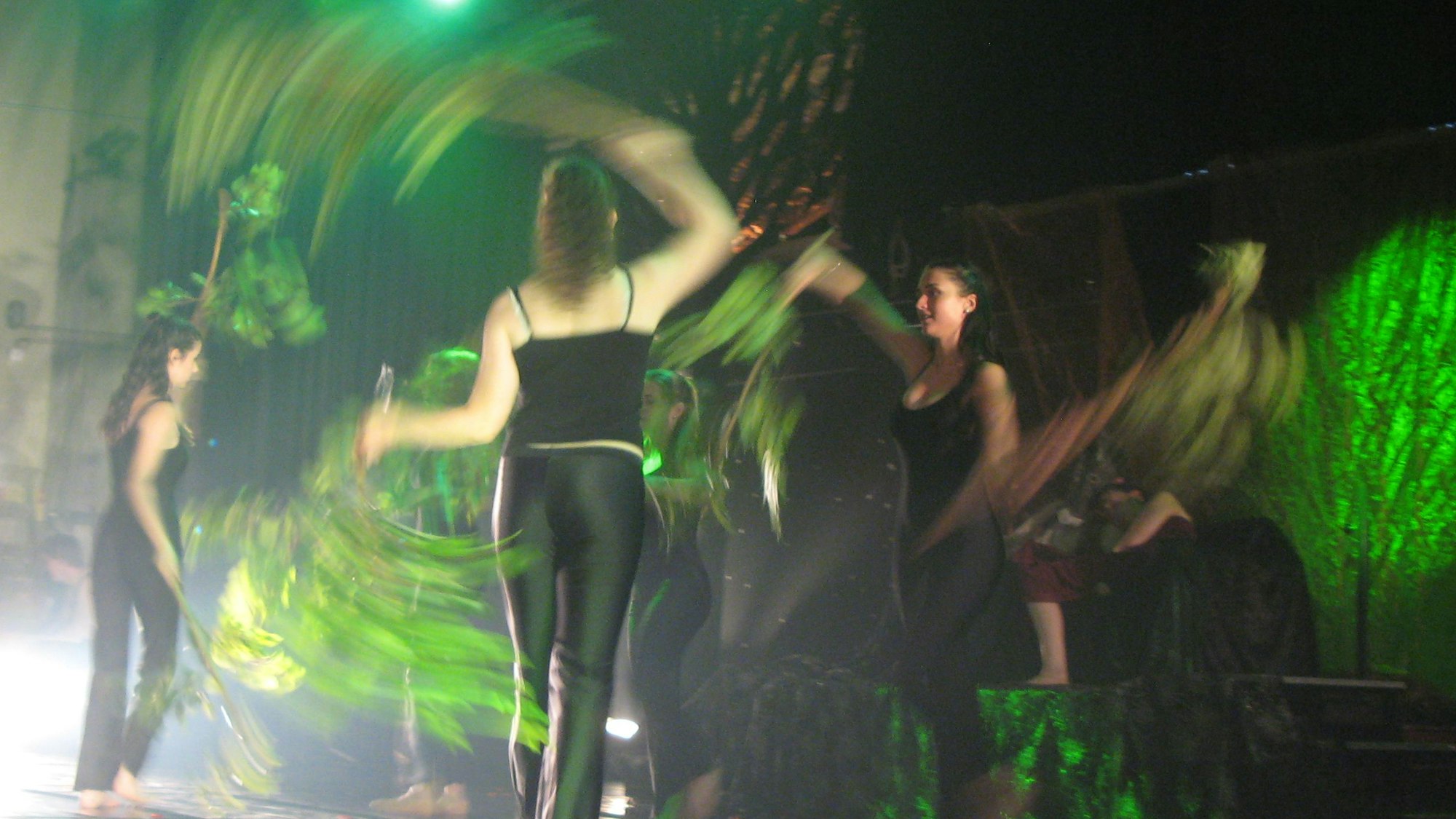 Schülerinnen tanzen auf einer Bühne und schwingen dabei belaubte Zweige.